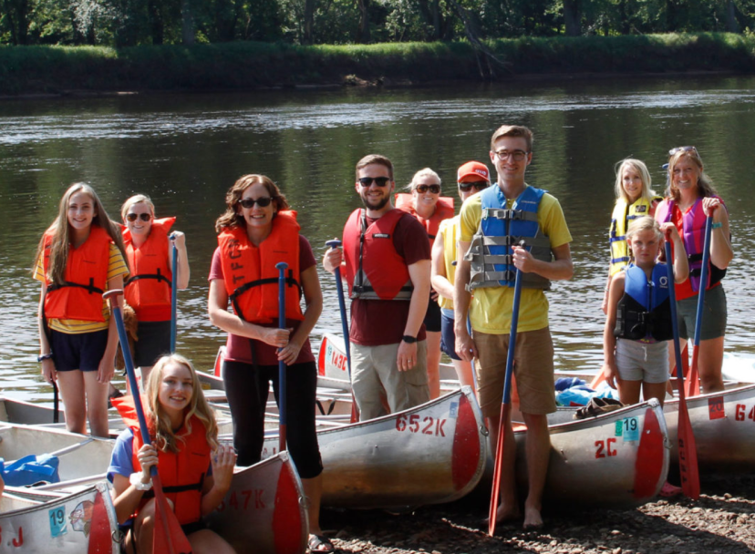 Group canoe trip on a calm river with adults and children wearing life jackets